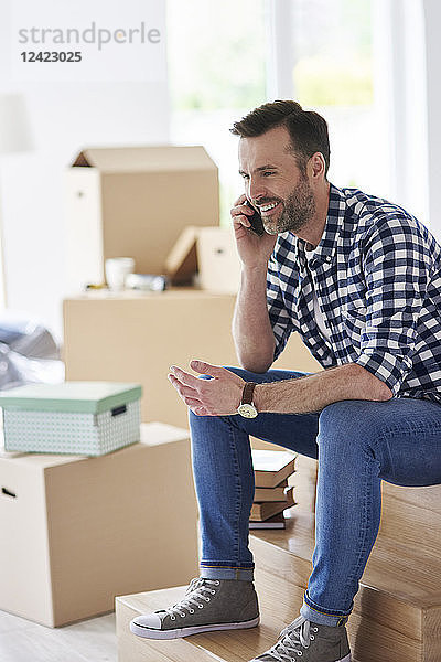 Smiling man moving into new flat talking on cell phone