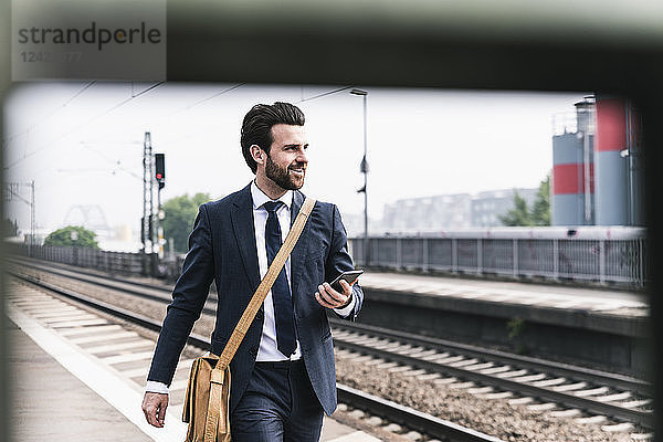 Smiling businessman with cell phone walking at the platform