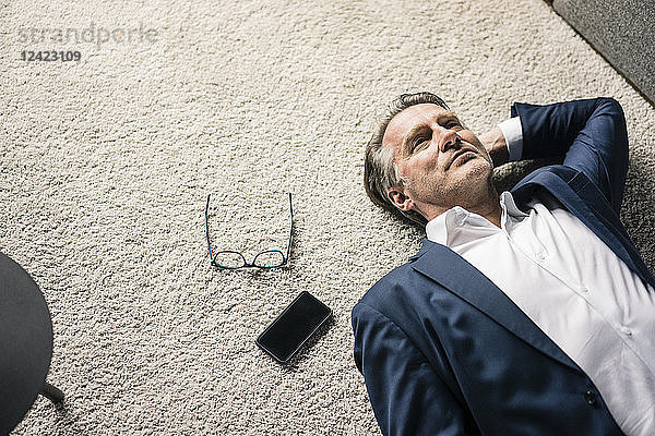 Mature businessman lying on carpet next to cell phone