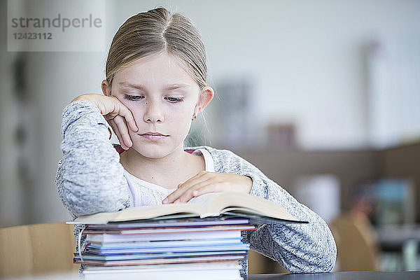 Schoolgirl reading book on table in school