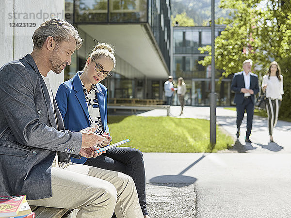 Colleagues with tablet sitting on bench outside office building