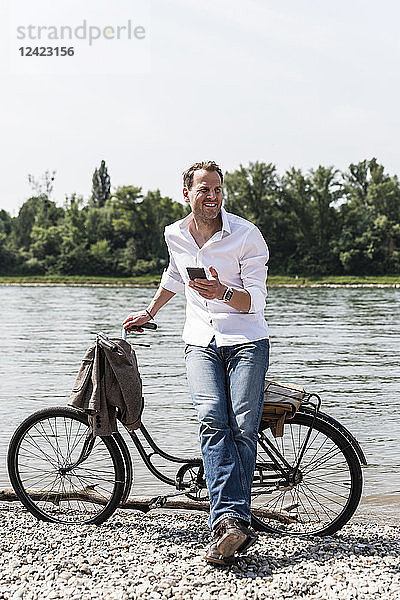 Mature man with bike using smartphone at Rhine riverbank