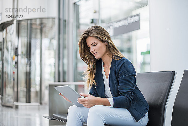Young businesswoman sitting at waiting area using tablet