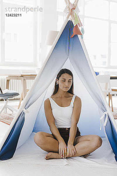 Young woman sitting cross-legged in a tent at home  with eyes closed