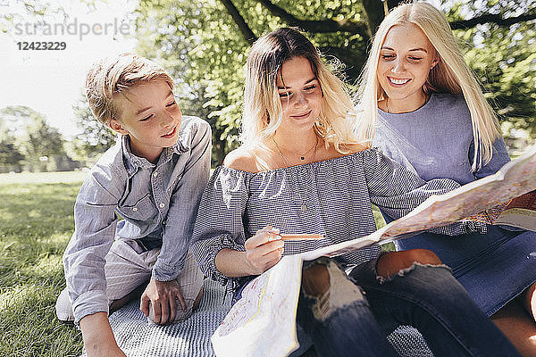 Two young women and a boy looking at map in a park