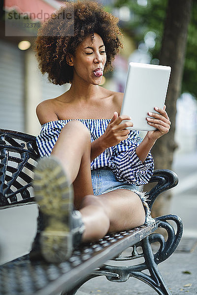 Portrait of young woman sitting on bench with tablet having video chat