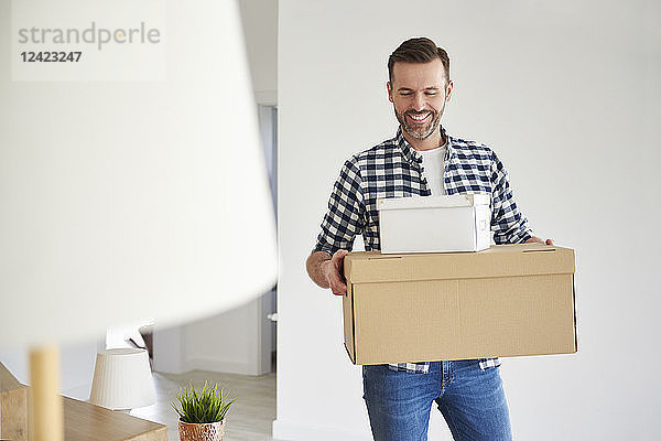 Happy man moving into new flat carrying cardboard box
