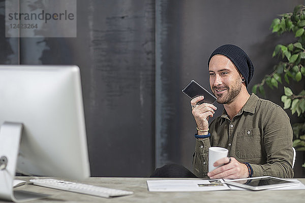 Smiling young man with cell phone at desk in office