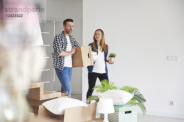 Happy couple moving into new flat carrying cardboard box and plant