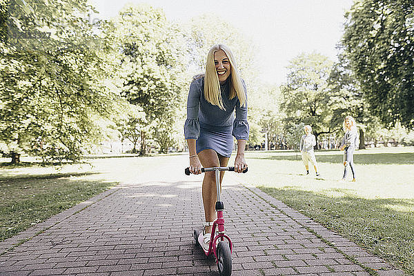 Happy young woman riding scooter in a park