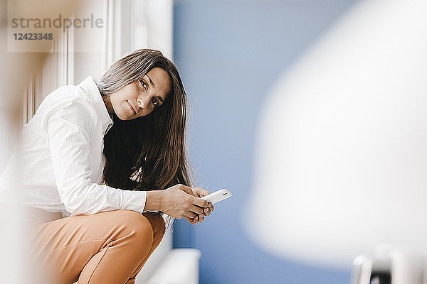 Young businesswoman sitting at window  using smartphone