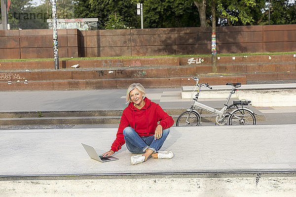 Senior woman wearing red hoodie using laptop outdoors