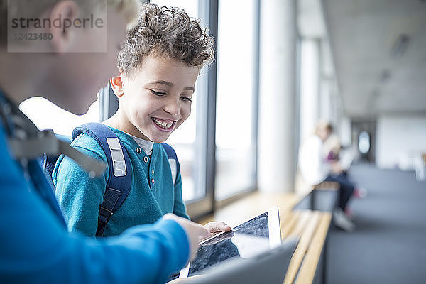 Smiling pupils sharing a tablet on school corridor