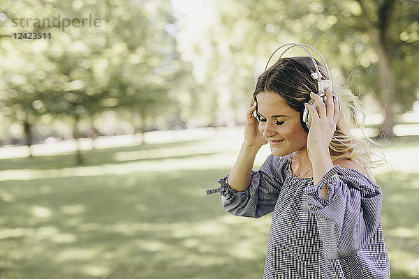 Smiling young woman in a park enjoying listening to music with headphones