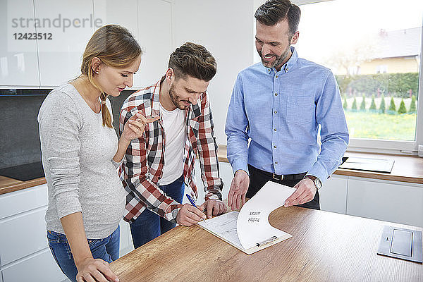 Couple with real estate agent signing contract in kitchen of new apartment