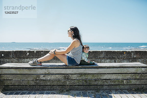France  mother and baby girl sitting back to back on a bench at beach promenade