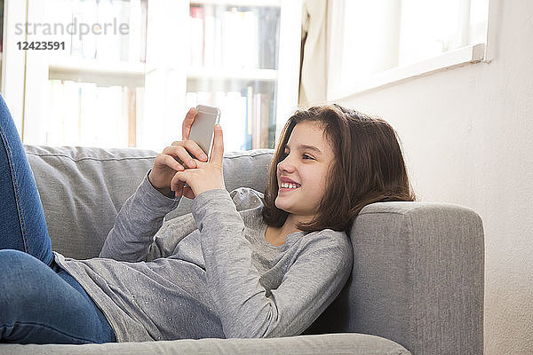 Smiling girl lying on couch at home using cell phone