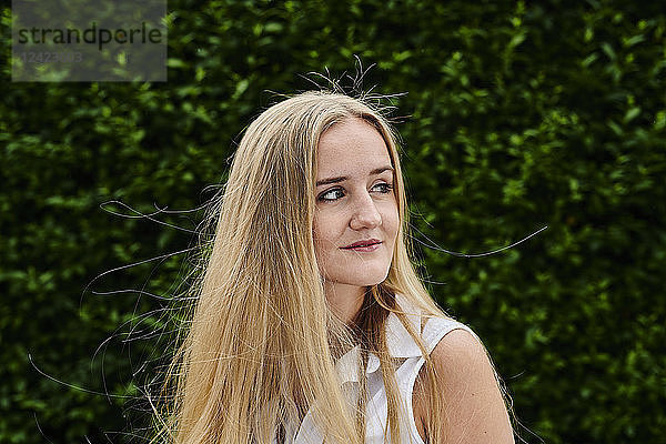 Blond young woman at a hedge looking sideways