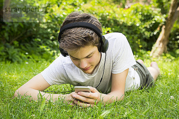 Boy lying on meadow listening music with headphones and smartphone