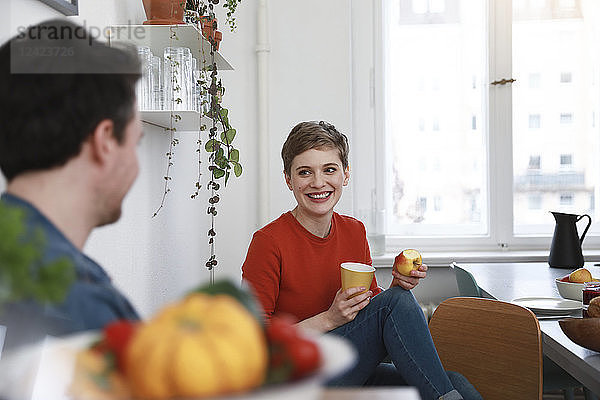 couple sitting in kitchen  talking  woman eating apple