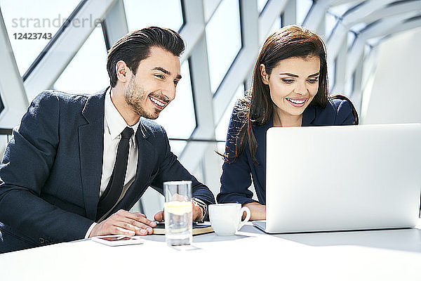 Smiling businesswoman and businessman using laptop at desk in modern office