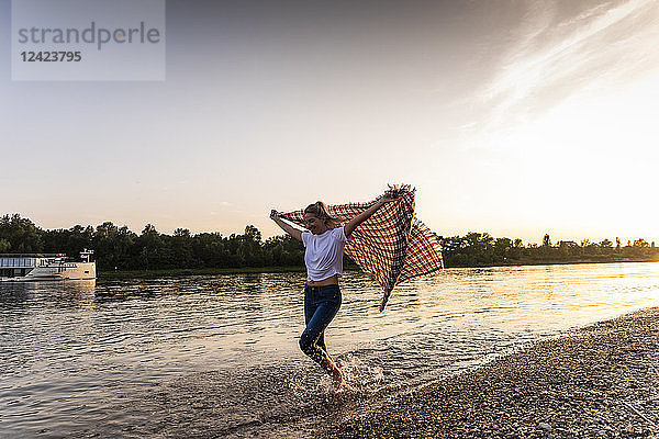 Young woman walking barefoot on riverside with blanket