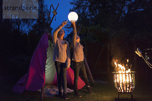 Two girls standing in front of tipi  holding lamp as moon