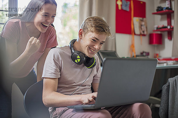 Happy teenage girl watching boy using laptop