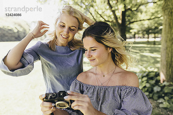 Two smiling young women with old-fashioned camera in a park