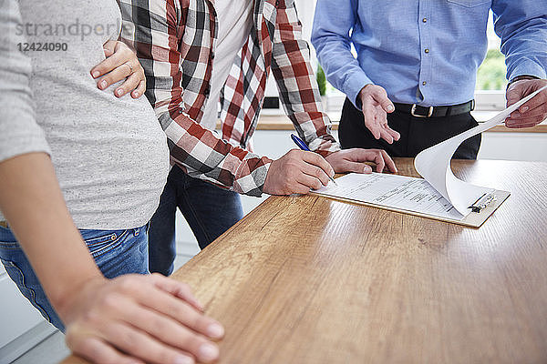 Couple with real estate agent signing contract in kitchen of new apartment