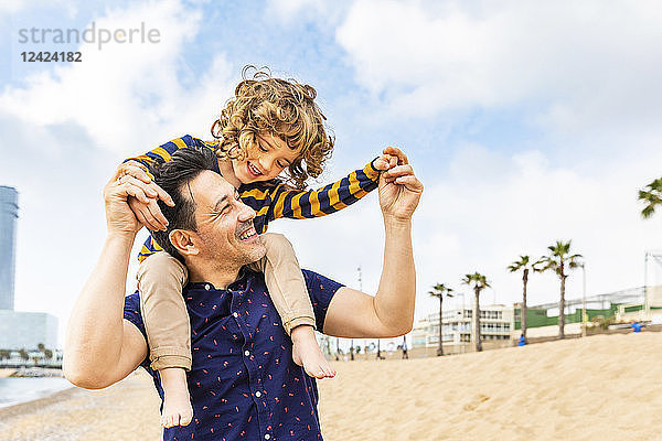 Spain  Barcelona  father with son on the beach giving a piggyback ride