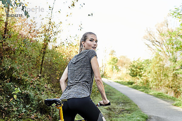 Rear view of sportive young woman with bicycle in a park