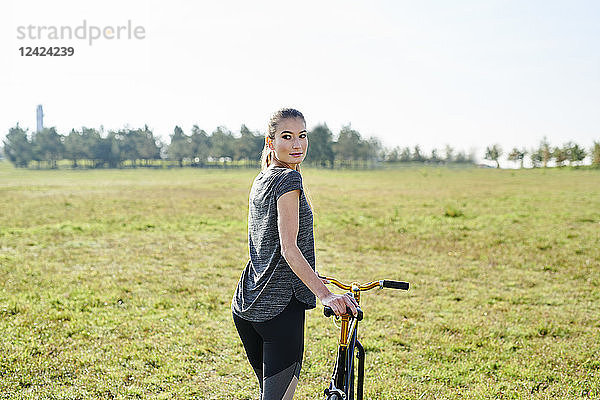 Sportive young woman with bicycle on a meadow