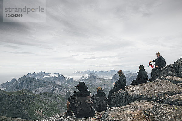 Norway  Lofoten  Moskenesoy  Young men sitting at Hermannsdalstinden  looking over Kjerkefjord