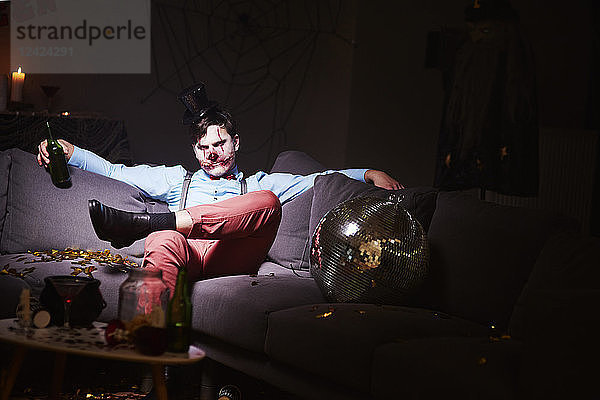 Man in Halloween costume sitting on couch after party  drinking beer