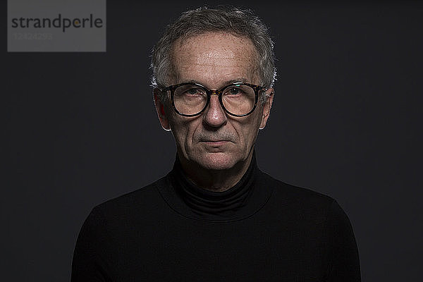 Portrait of serious senior man wearing glasses in front of dark background
