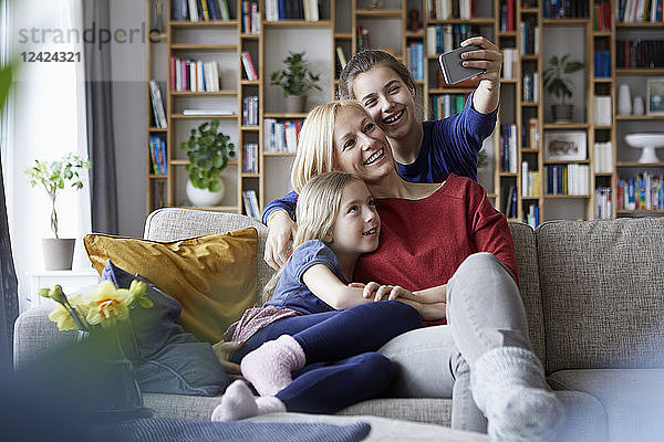 Mother and her daughters sitting on couch taking smartphone selfies