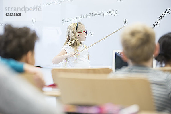 Schoolgirl explaining formula at whiteboard in class