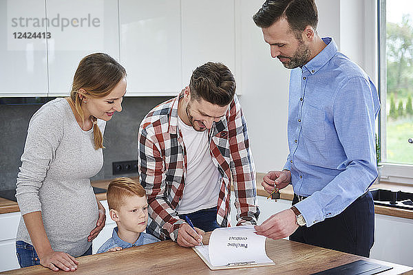 Family with real estate agent signing contract in kitchen of new apartment