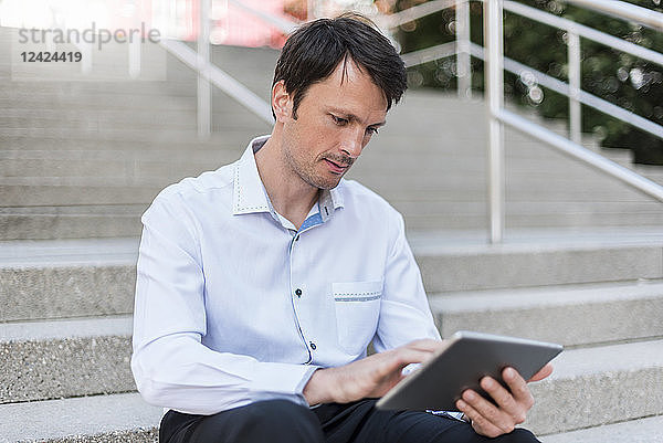 Businessman sitting on stairs using tablet
