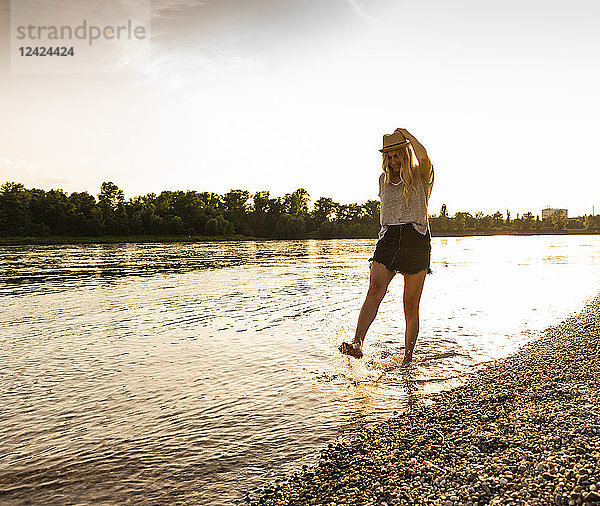 Young woman walking barefoot on riverside in the evening