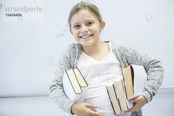 Portrait of happy schoolgirl carrying books in class