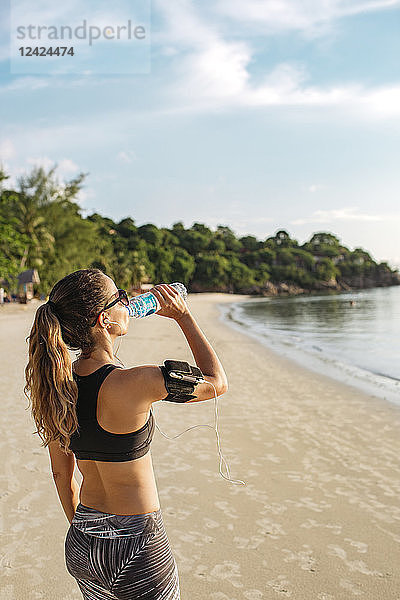 Thailand  Koh Phangan  Sportive woman drinking water on the beach