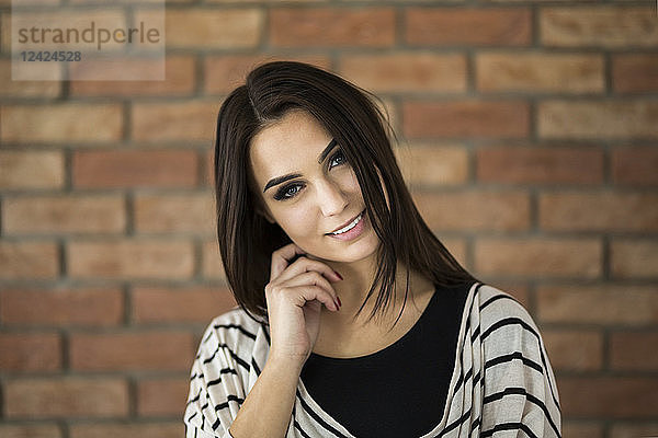 Portrait of smiling young woman with long brown hair in front of brick wall