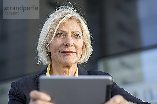 Portrait of smiling senior businesswoman with tablet outdoors