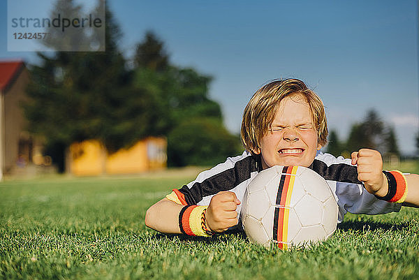 Boy in German soccer shirt lying on grass  keeping fingers crossed for world championship
