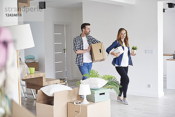 Couple moving into new flat carrying cardboard box and plant