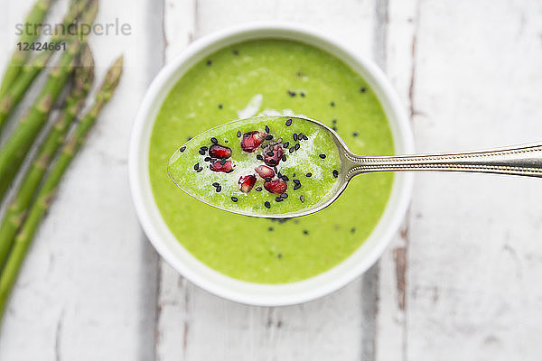 Green asparagus soup with pomegranate seeds and black sesame on spoon  close-up