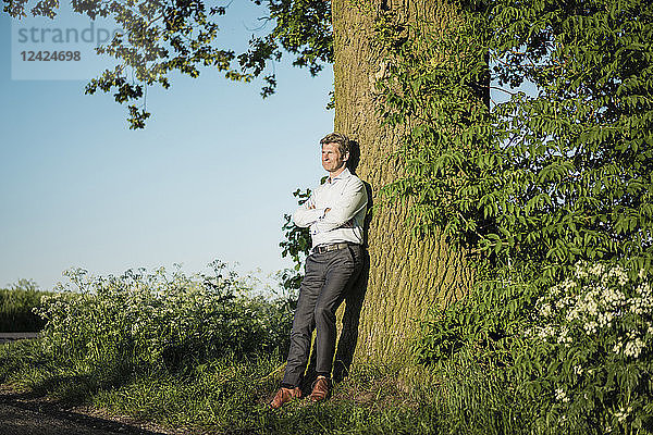 Businessman leaning on tree