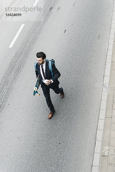 Businessman with takeaway coffee and skateboard walking on the street